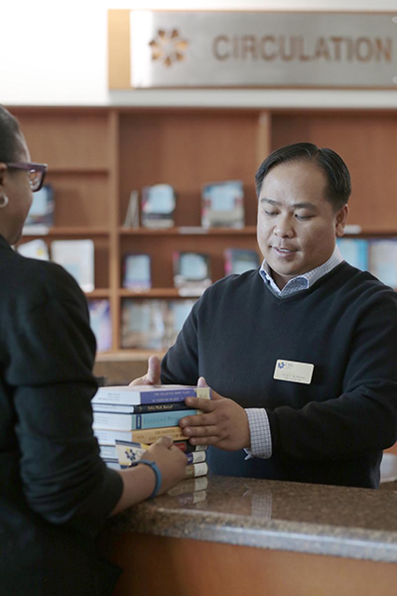 A photo of a CSN student checking out a book at the West Charleston campus