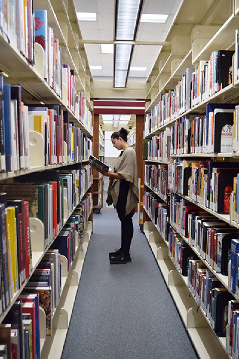 A photo of a student standing between bookshelves reading a book